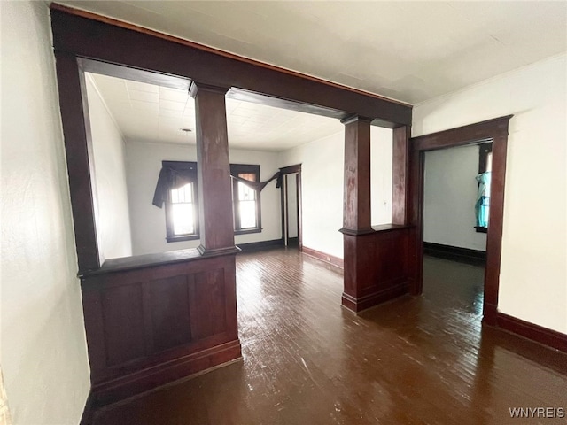 empty room featuring decorative columns, baseboards, and wood finished floors