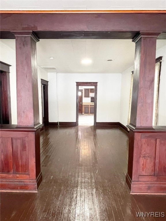 empty room featuring baseboards, hardwood / wood-style floors, and ornate columns