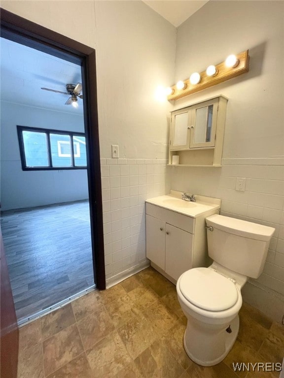 half bath featuring tile walls, toilet, a ceiling fan, wainscoting, and vanity