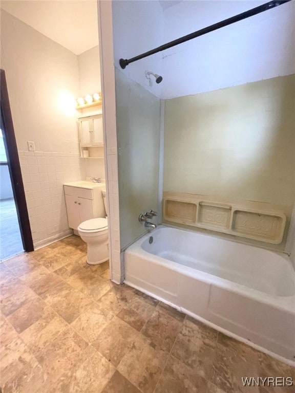 full bath featuring toilet, a wainscoted wall, vanity, bathing tub / shower combination, and tile walls