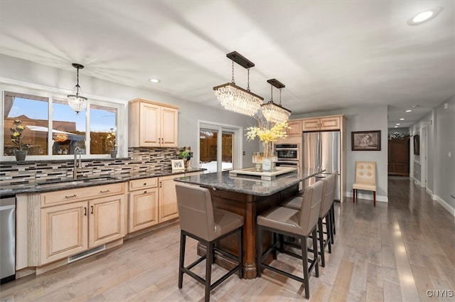 kitchen with stainless steel appliances, visible vents, backsplash, light brown cabinetry, and a sink