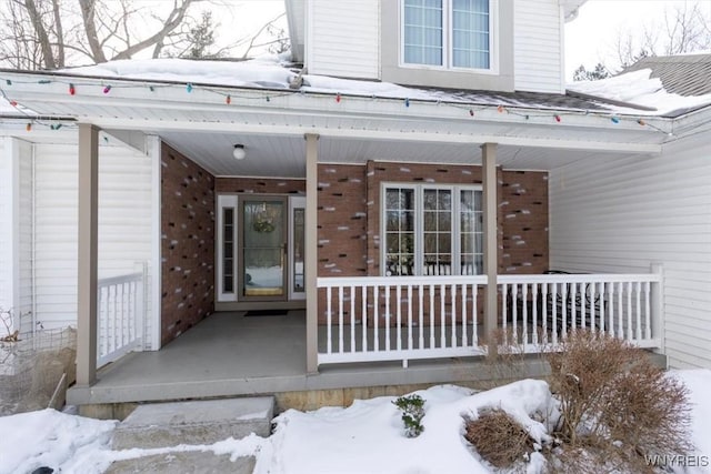 snow covered property entrance with a porch and brick siding