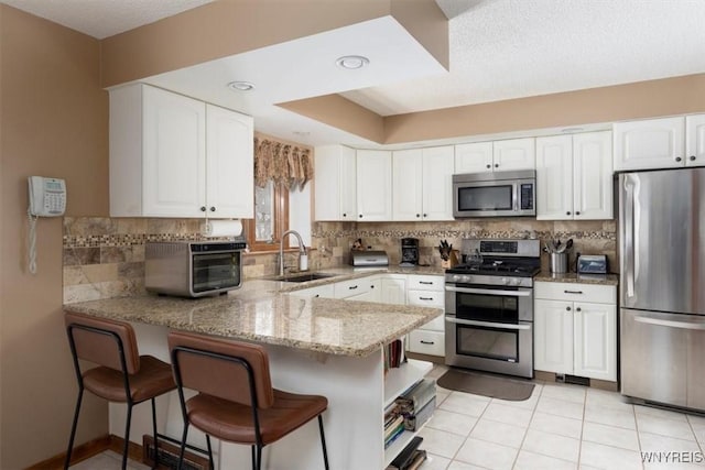 kitchen with light stone counters, a peninsula, stainless steel appliances, white cabinetry, and a sink