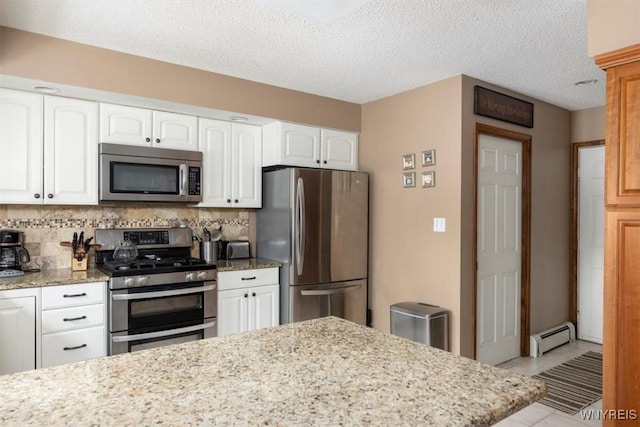 kitchen with stainless steel appliances, tasteful backsplash, baseboard heating, white cabinets, and light stone countertops