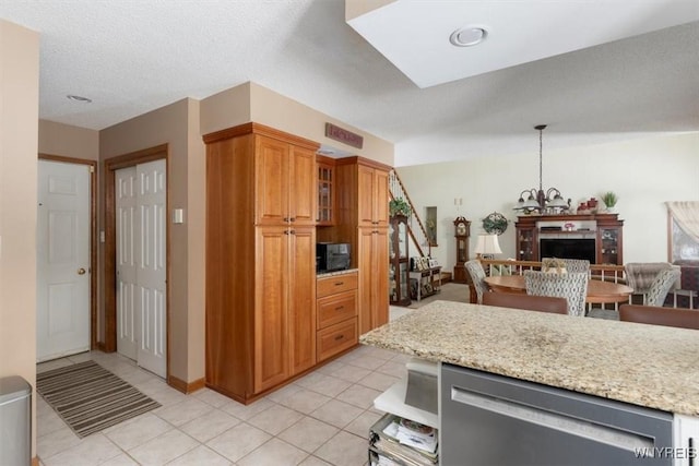 kitchen featuring brown cabinetry, glass insert cabinets, light tile patterned flooring, light stone countertops, and a chandelier