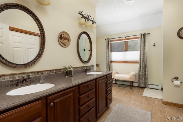 bathroom featuring double vanity, a sink, baseboard heating, and wood finished floors