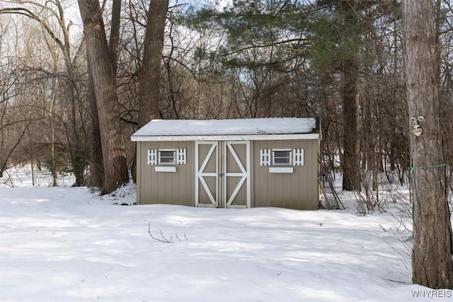 snow covered structure featuring an outbuilding and a storage shed