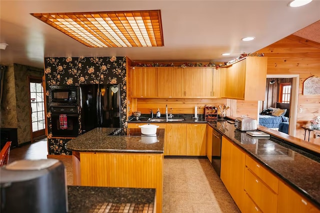 kitchen featuring wood walls, a sink, light brown cabinetry, black appliances, and dark stone countertops