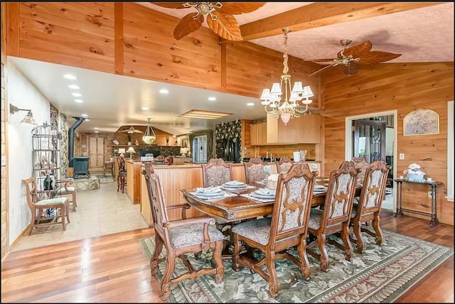 dining room featuring light wood-type flooring, a wood stove, wood walls, and ceiling fan with notable chandelier