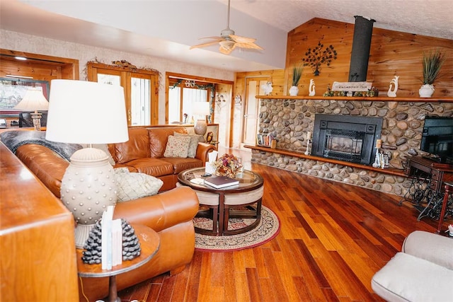 living room featuring ceiling fan, vaulted ceiling, a stone fireplace, and wood finished floors