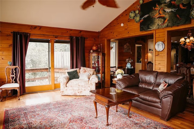 living room featuring lofted ceiling, wood walls, wood finished floors, and a chandelier