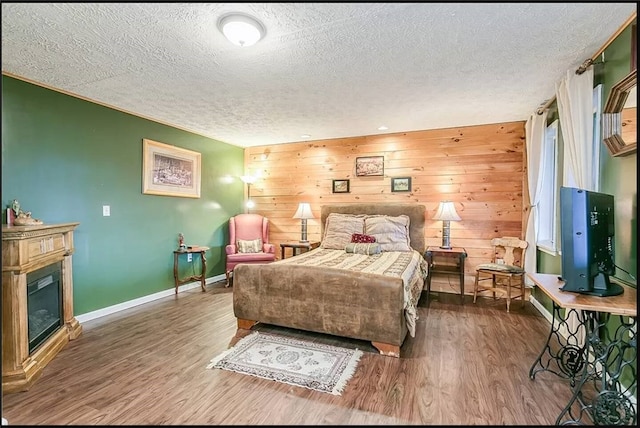 bedroom with a textured ceiling, baseboards, wood finished floors, and a glass covered fireplace