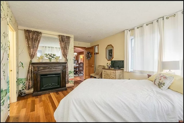 bedroom featuring a textured ceiling, arched walkways, a fireplace, and wood finished floors