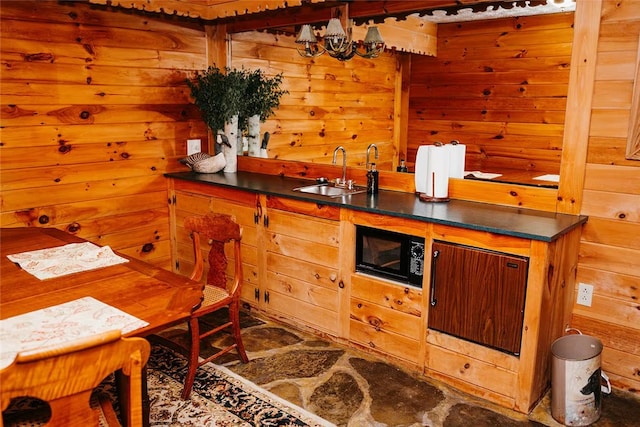 kitchen featuring dark countertops, an inviting chandelier, a sink, wooden walls, and black microwave