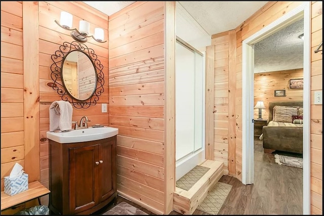 full bath featuring a textured ceiling, wood walls, vanity, and a stall shower