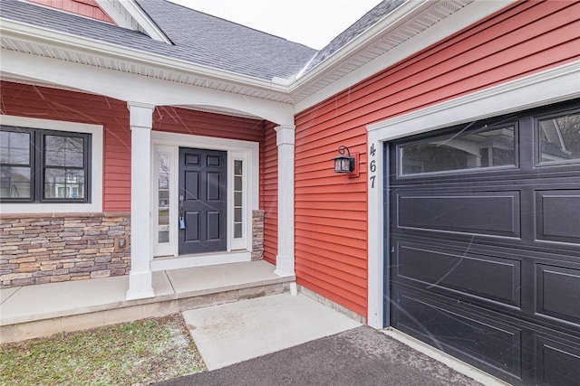 doorway to property with covered porch, stone siding, roof with shingles, and an attached garage