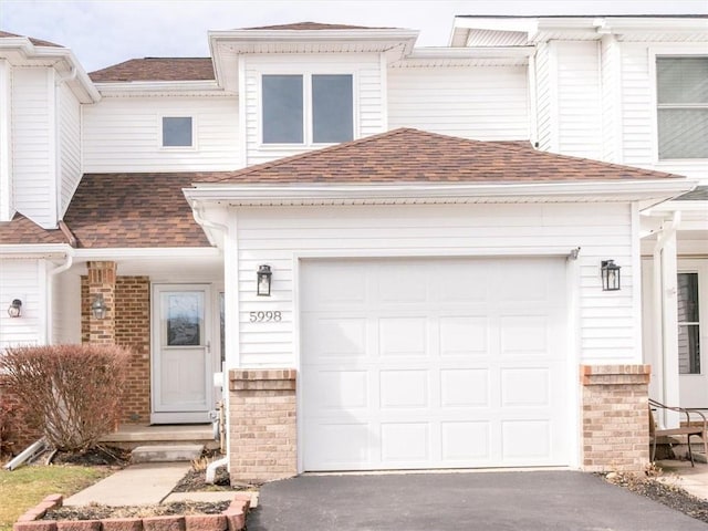 multi unit property featuring driveway, brick siding, a garage, and roof with shingles