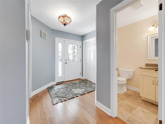 entryway featuring light wood-style floors, visible vents, a textured ceiling, and baseboards