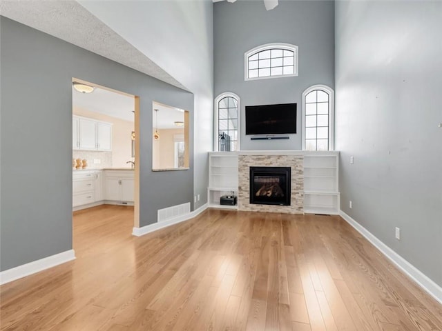 unfurnished living room featuring light wood-type flooring, baseboards, visible vents, and a glass covered fireplace