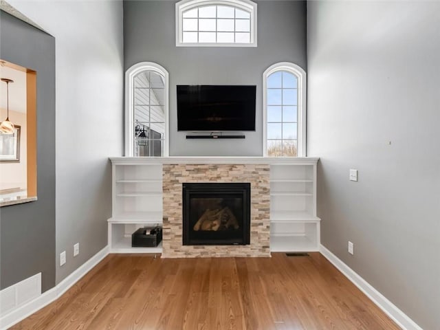 unfurnished living room with visible vents, baseboards, wood finished floors, and a glass covered fireplace