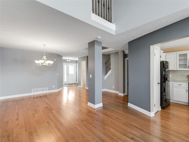 unfurnished living room featuring visible vents, stairway, a chandelier, light wood-type flooring, and baseboards