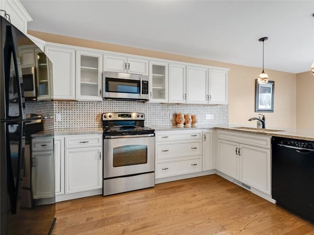 kitchen featuring a sink, white cabinets, light wood-style floors, black appliances, and decorative light fixtures