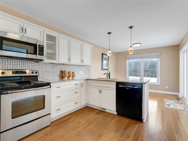 kitchen with light wood finished floors, tasteful backsplash, a peninsula, stainless steel appliances, and a sink