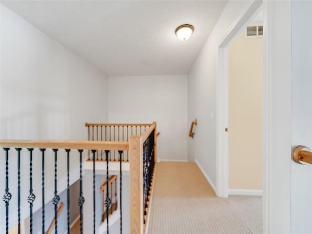 hallway with carpet, visible vents, baseboards, and an upstairs landing