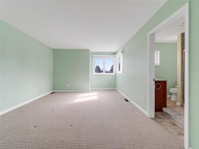 carpeted spare room with visible vents, a textured ceiling, and baseboards