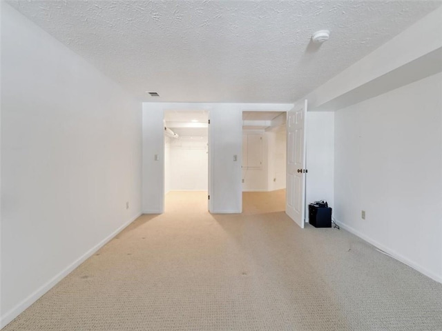 spare room with a textured ceiling, baseboards, visible vents, and light colored carpet