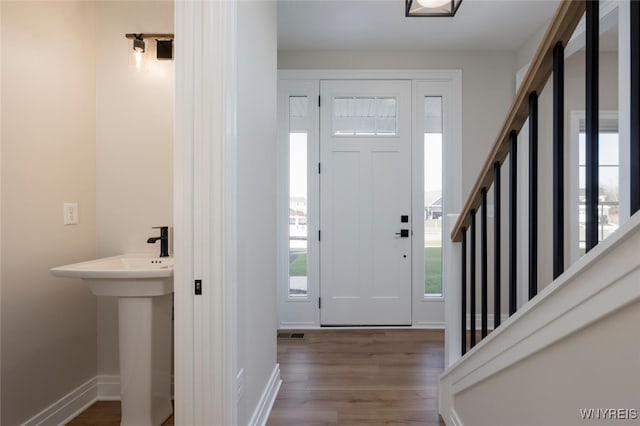 foyer with baseboards, visible vents, stairway, and wood finished floors