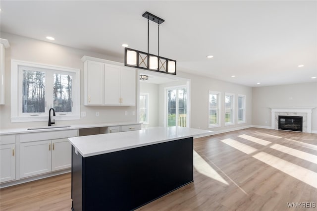 kitchen with light countertops, a sink, light wood-style flooring, and a high end fireplace