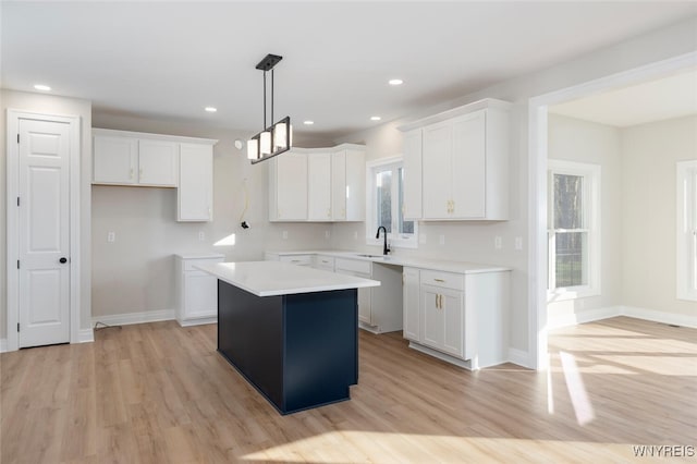 kitchen with light wood-type flooring, a sink, white cabinetry, and a center island