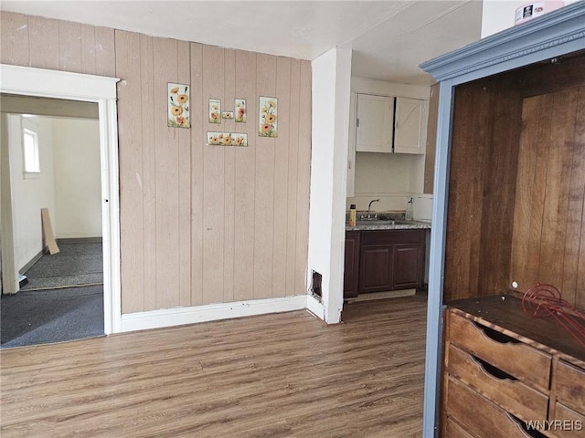 unfurnished dining area featuring a sink, wood walls, wood finished floors, and baseboards