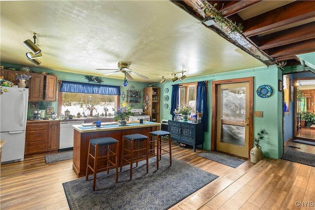 kitchen featuring white appliances, a sink, light wood-style floors, a center island, and a kitchen bar