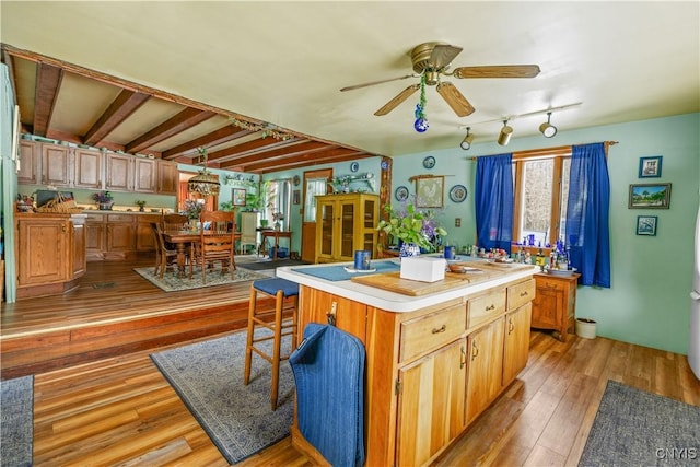 kitchen with ceiling fan, light wood-style flooring, a kitchen island, a breakfast bar, and light countertops