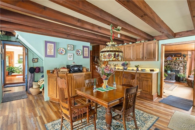 dining space with light wood-style floors, a wood stove, and beamed ceiling