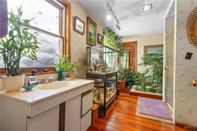 bathroom with a healthy amount of sunlight, wallpapered walls, hardwood / wood-style flooring, and vanity