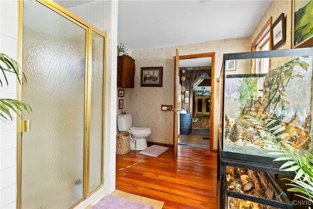 bathroom with a stall shower, wood finished floors, toilet, and wallpapered walls