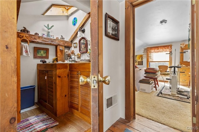 hallway with vaulted ceiling with skylight, hardwood / wood-style floors, carpet flooring, and visible vents