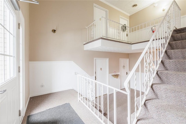 stairway with a towering ceiling, carpet, baseboards, and ornamental molding