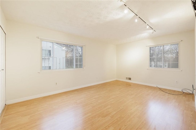 spare room with light wood-type flooring, visible vents, and baseboards