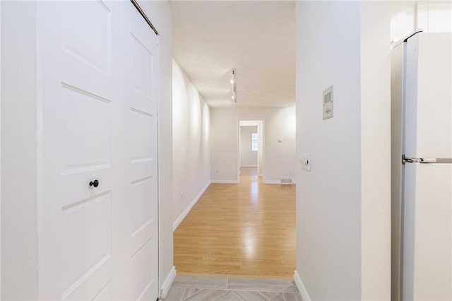 hallway with baseboards, visible vents, and light wood-style floors