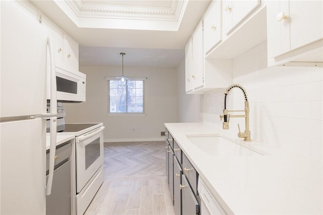 kitchen featuring light countertops, white cabinets, a sink, white appliances, and baseboards