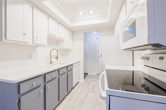 kitchen with white appliances, a sink, backsplash, a tray ceiling, and crown molding