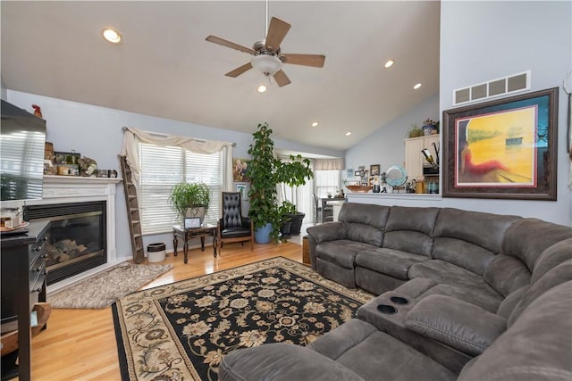 living room featuring a glass covered fireplace, wood finished floors, visible vents, and a healthy amount of sunlight