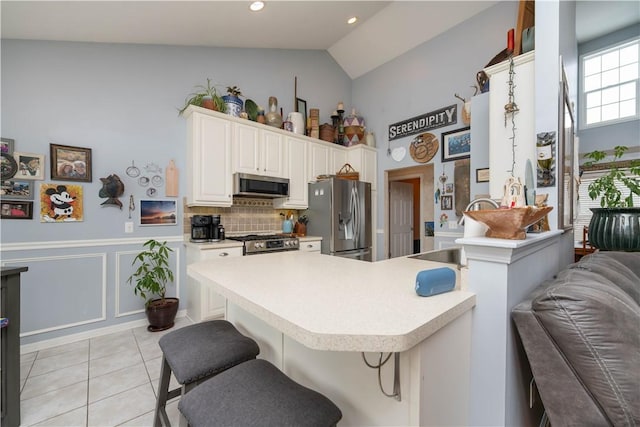 kitchen featuring light tile patterned flooring, stainless steel appliances, light countertops, wainscoting, and a kitchen bar