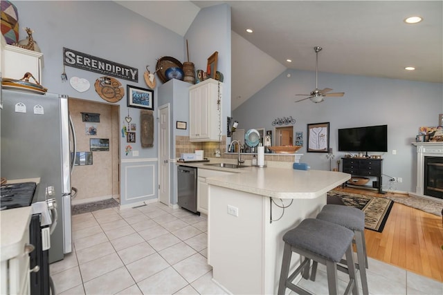 kitchen with light tile patterned floors, open floor plan, a peninsula, stainless steel appliances, and a sink