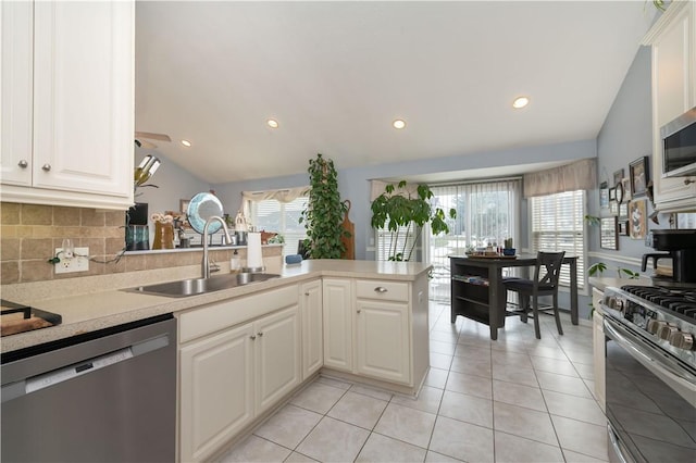 kitchen with a sink, vaulted ceiling, light countertops, appliances with stainless steel finishes, and decorative backsplash