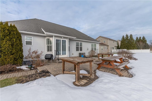 snow covered rear of property featuring a patio, a shingled roof, and outdoor dining area